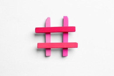 Photo of Hashtag symbol of pink chalk pieces on white background, top view