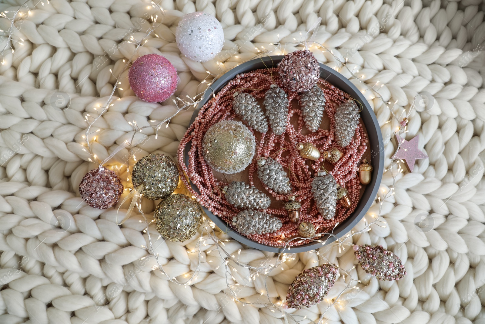 Photo of Beautiful Christmas tree baubles and fairy lights on white knitted fabric, flat lay