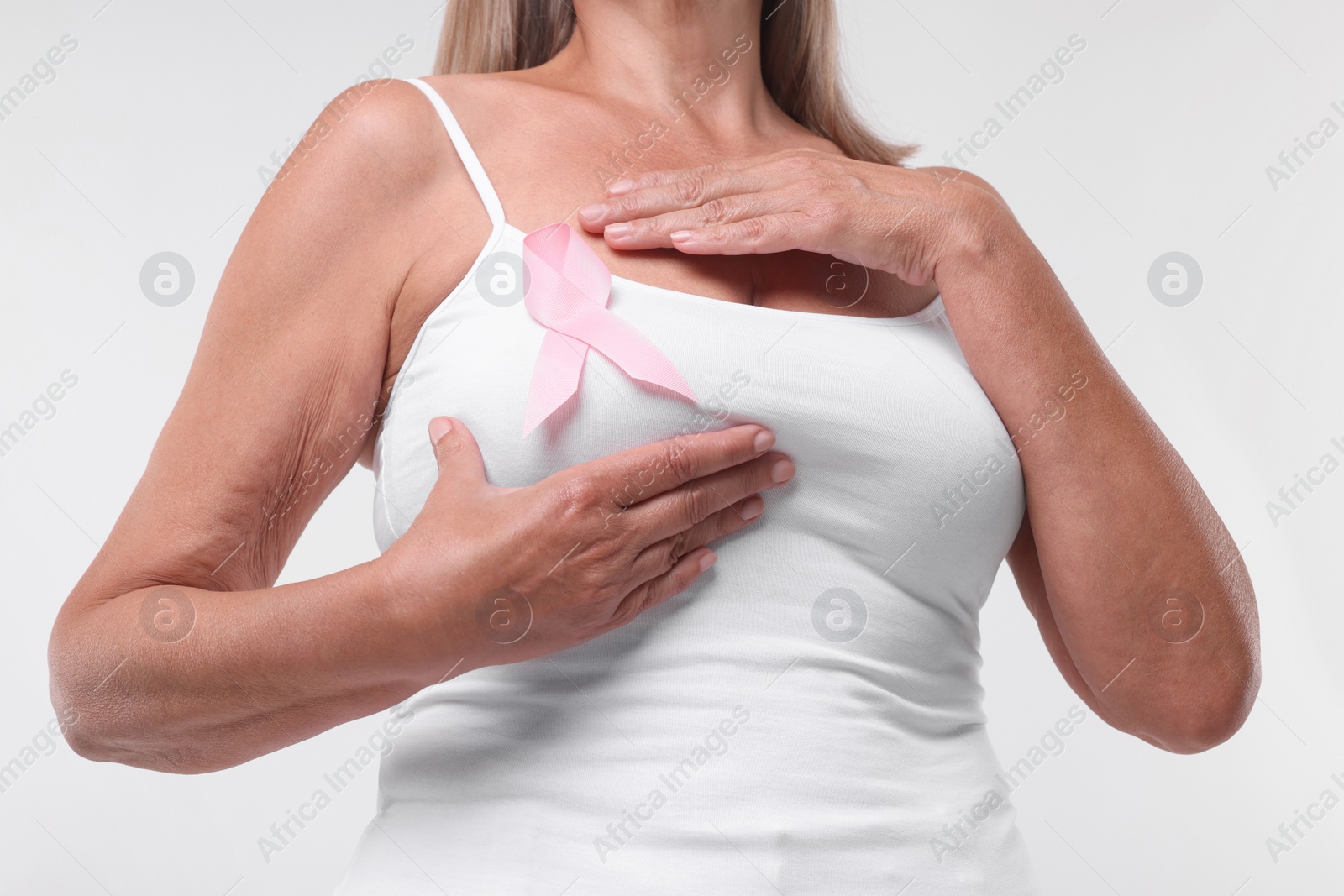 Photo of Woman with pink ribbon on white background, closeup. Breast cancer awareness