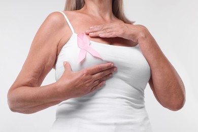 Woman with pink ribbon on white background, closeup. Breast cancer awareness