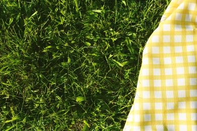 Checkered picnic tablecloth on fresh green grass, top view. Space for text