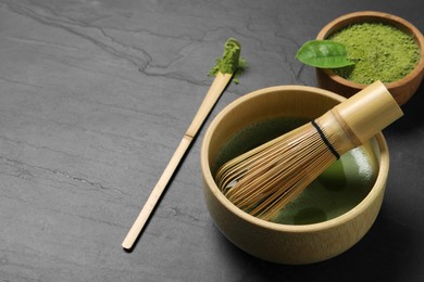 Photo of Fresh matcha tea, bamboo whisk, spoon and green powder on black table, closeup. Space for text