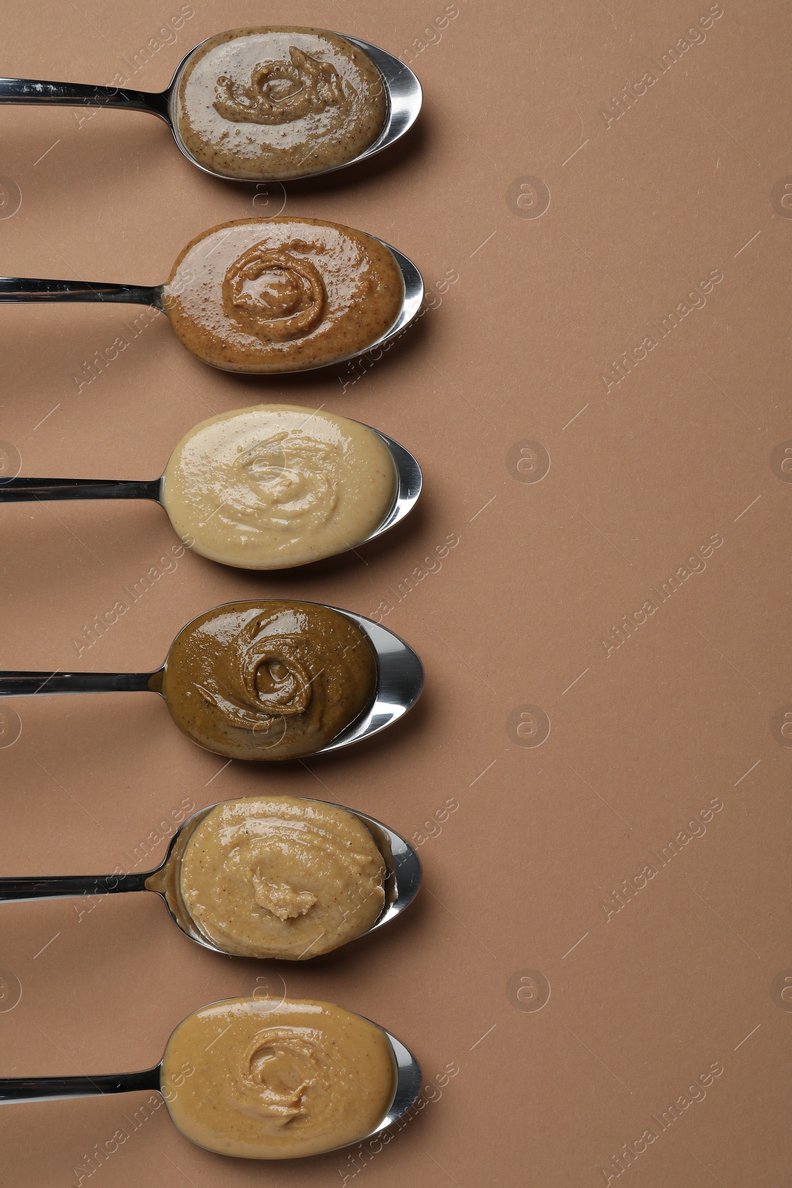 Photo of Tasty nut butters in spoons on light brown table, flat lay. Space for text