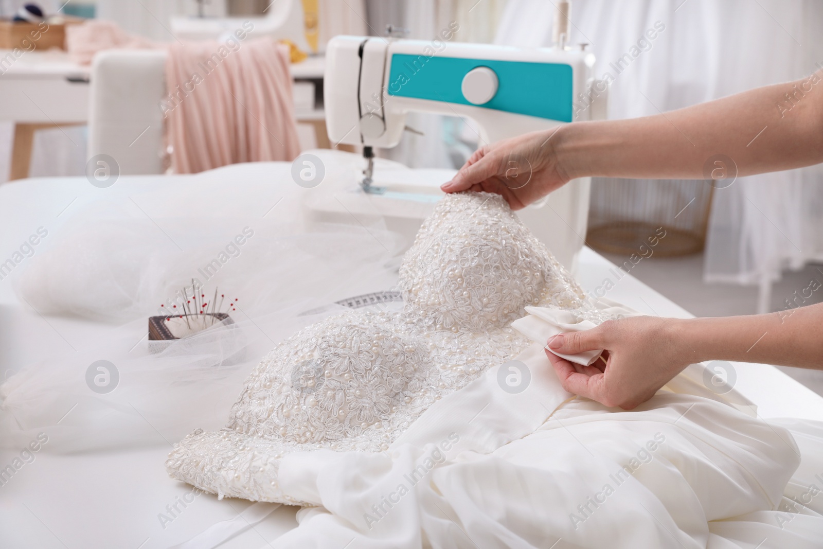 Photo of Dressmaker creating beautiful wedding dress with embroidered bustline and bow at table in workshop, closeup