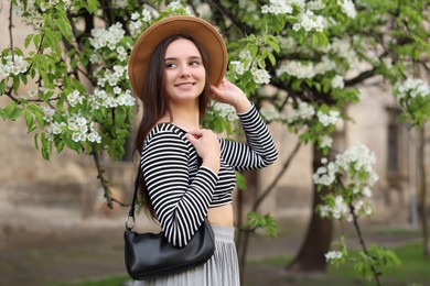 Beautiful woman in hat near blossoming tree on spring day