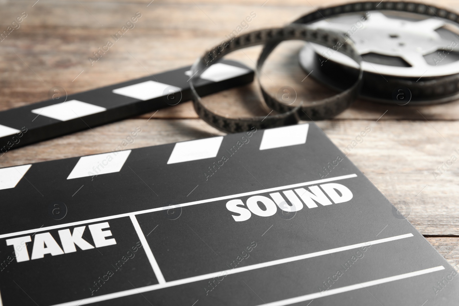 Photo of Clapperboard and reel on wooden table, closeup. Cinema production