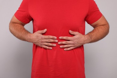 Photo of Man suffering from stomach pain on grey background, closeup