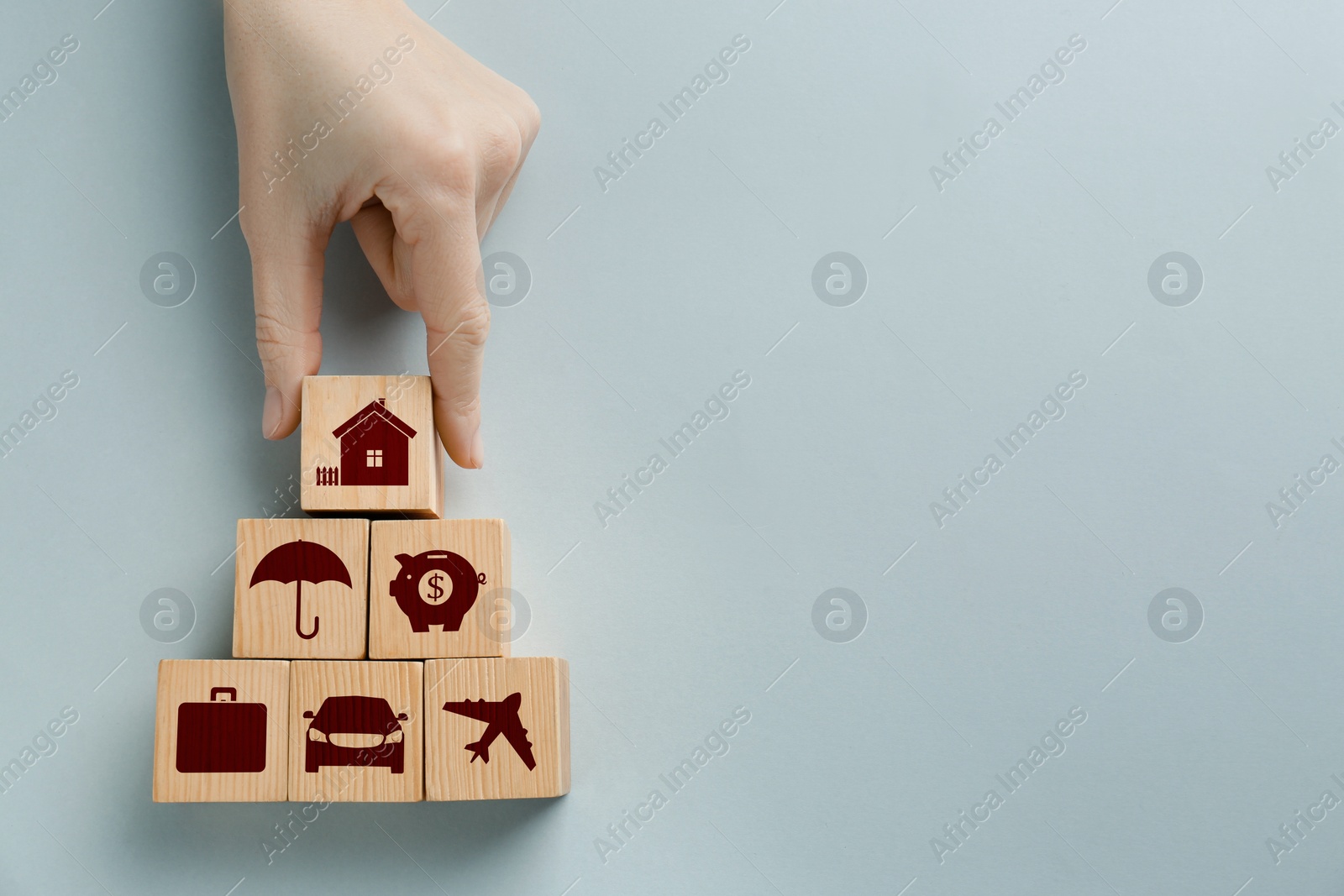 Image of Woman building pyramid of wooden cubes with different icons on light background, top view. Insurance concept