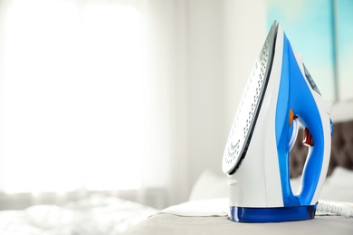 Modern electric iron on board indoors, space for text. Household appliance