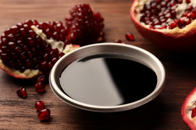 Glass bowl of tasty pomegranate sauce and fresh ripe fruit on wooden table, closeup