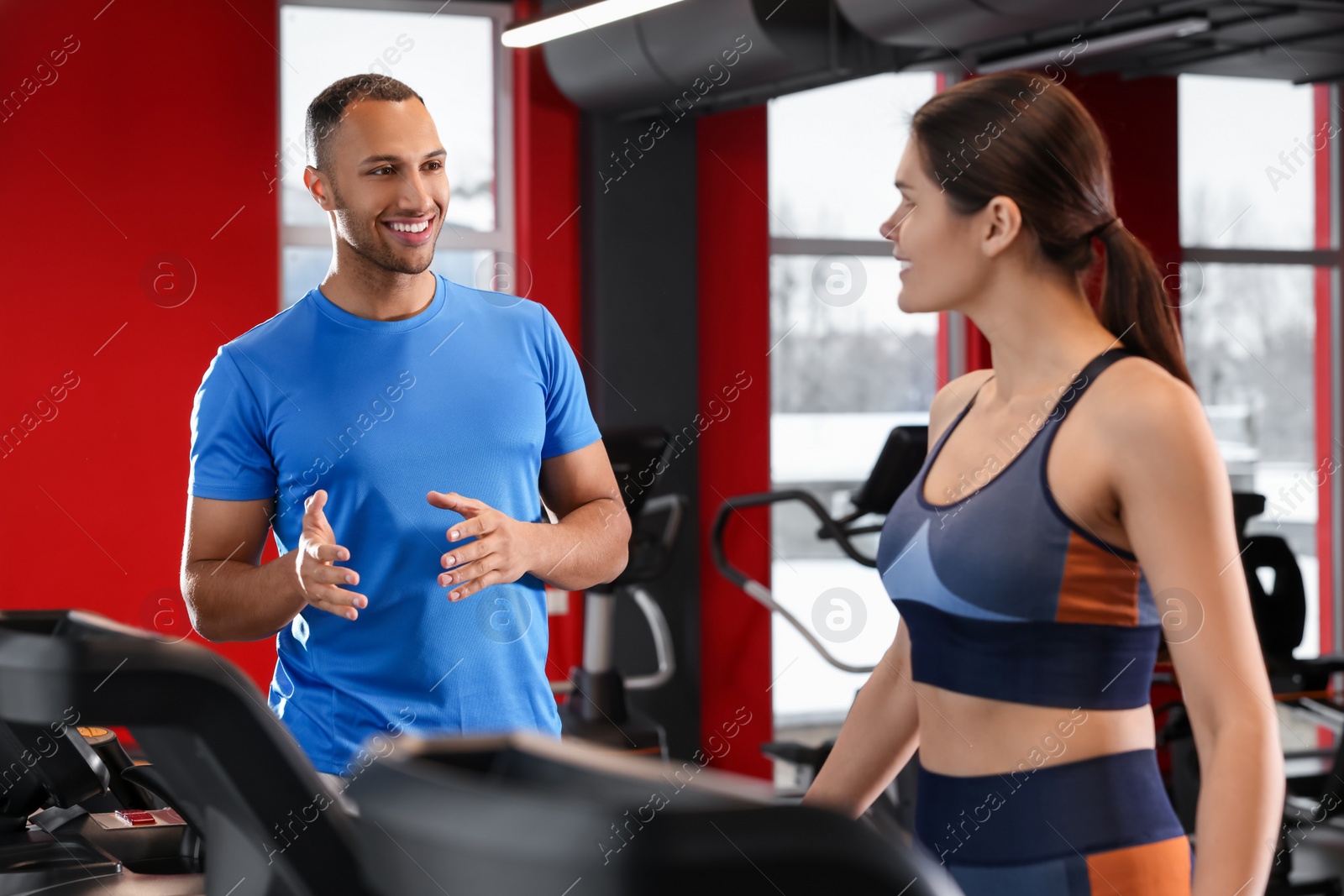 Photo of Happy trainer explaining woman how to do exercise properly in modern gym