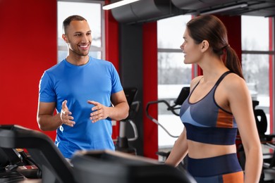 Photo of Happy trainer explaining woman how to do exercise properly in modern gym