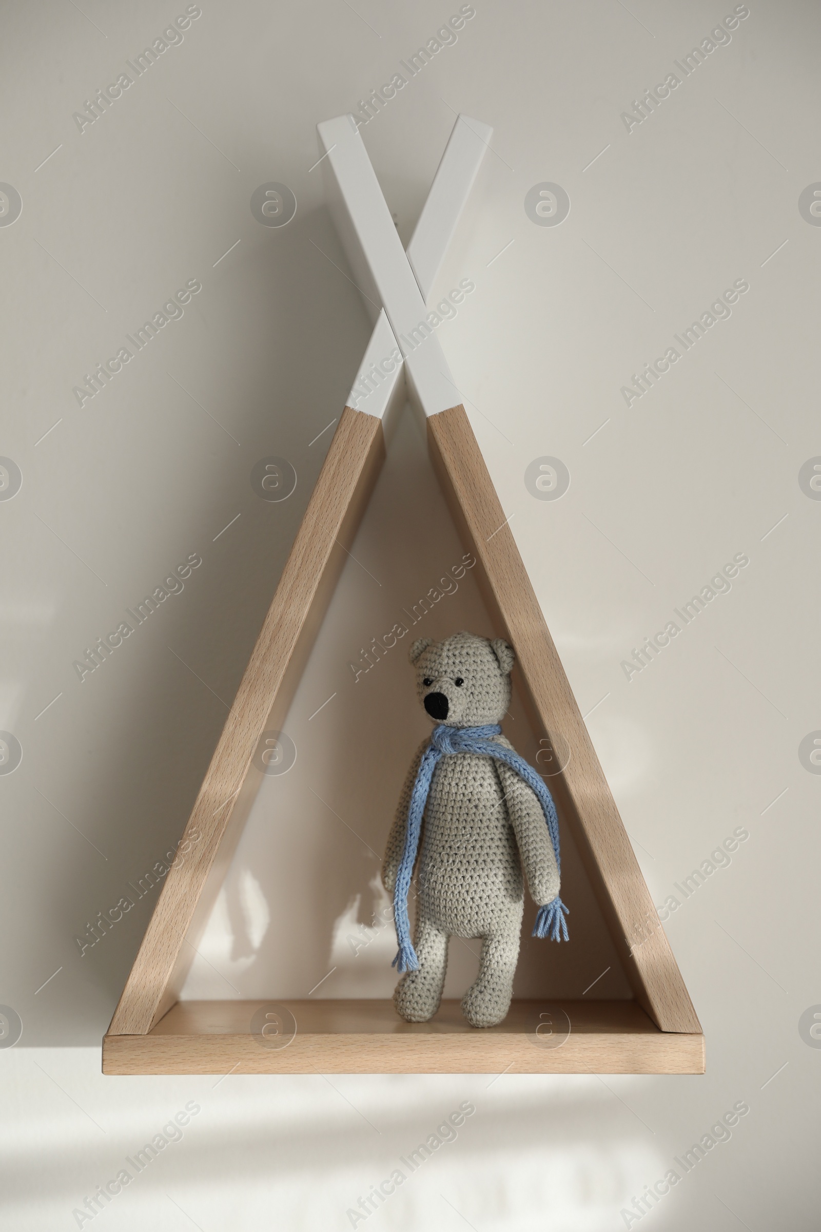 Photo of Wigwam shaped shelf with toy bear on white wall indoors. Children's room interior