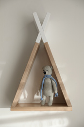 Wigwam shaped shelf with toy bear on white wall indoors. Children's room interior