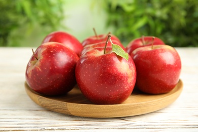 Photo of Wooden plate with ripe juicy red apples on white table against blurred background