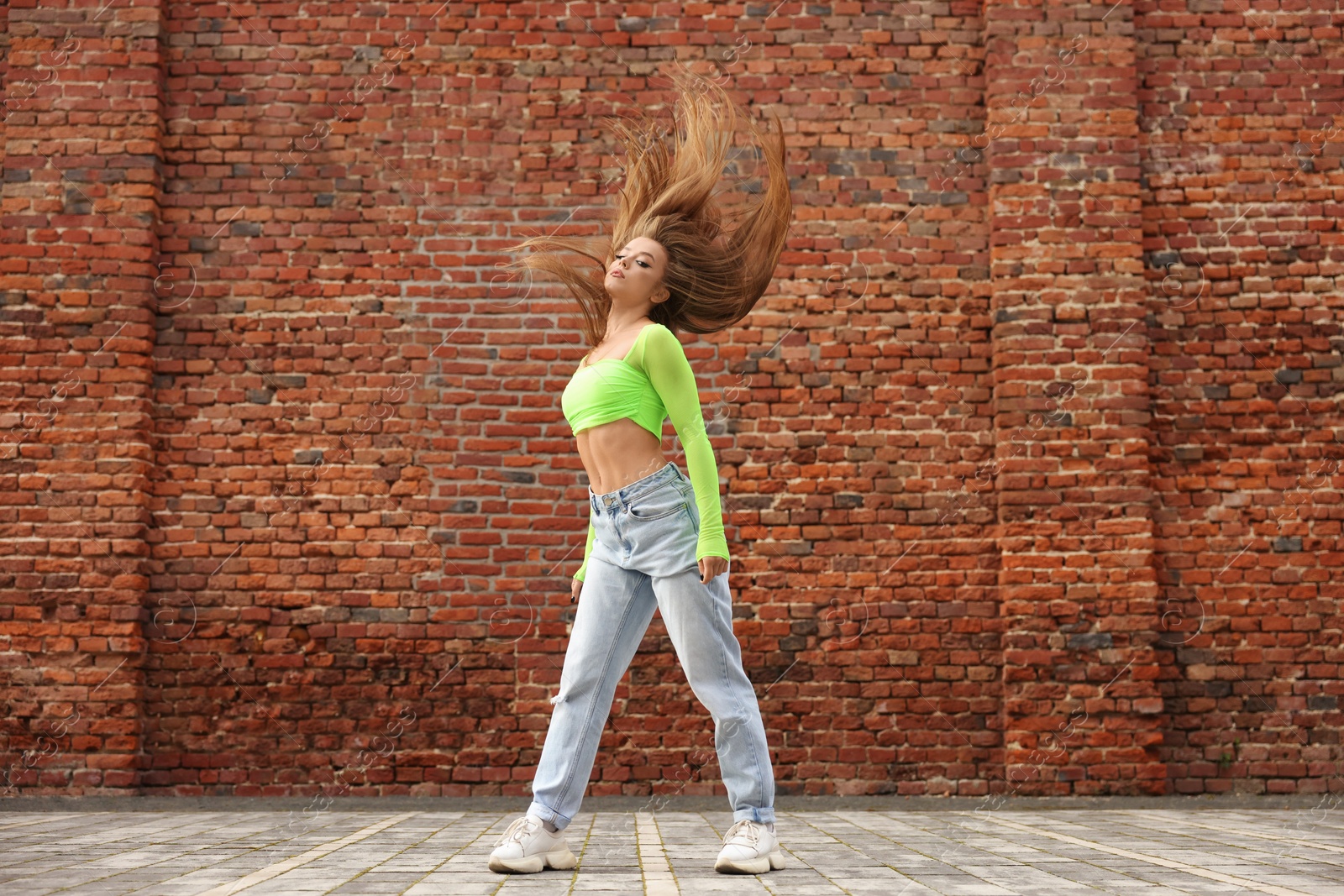 Photo of Beautiful young woman dancing hip hop near brick wall outdoors