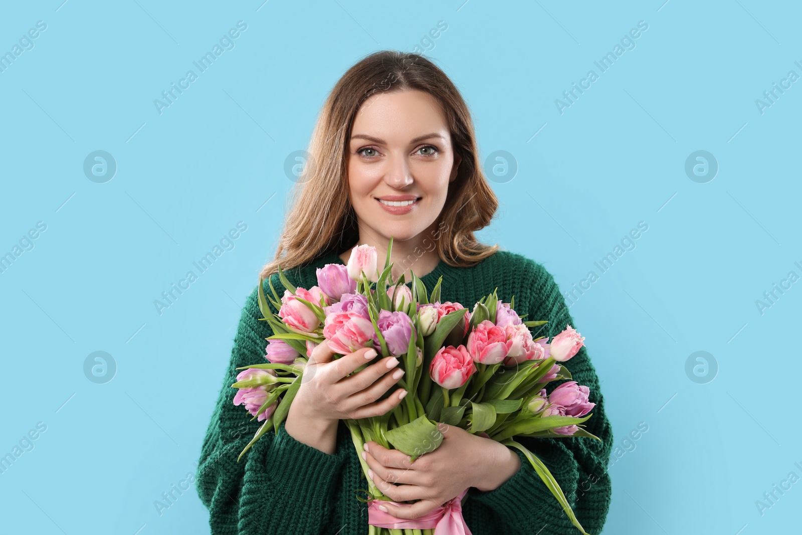 Photo of Happy young woman with bouquet of beautiful tulips on light blue background