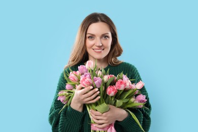 Happy young woman with bouquet of beautiful tulips on light blue background