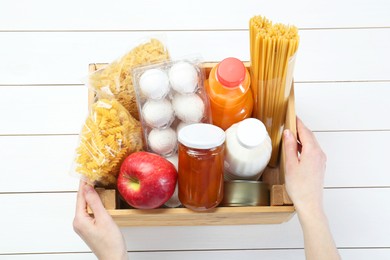 Photo of Humanitarian aid. Woman with food products for donation at white wooden table, top view