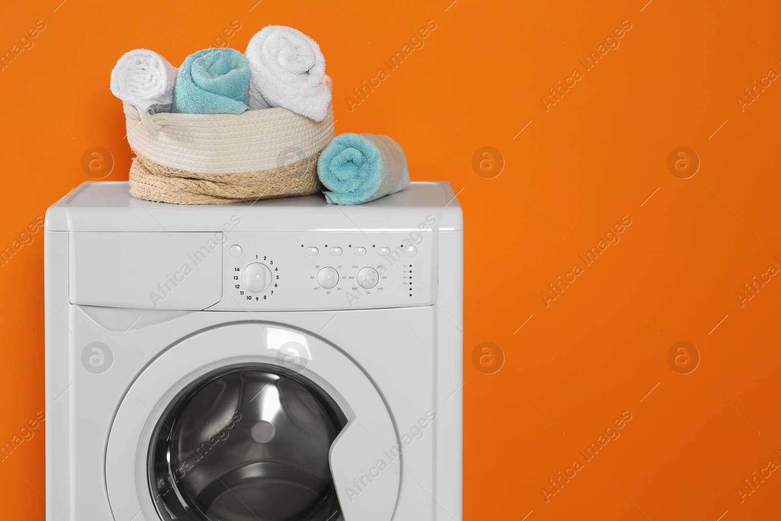 Photo of Washing machine with clean towels on orange background, space for text