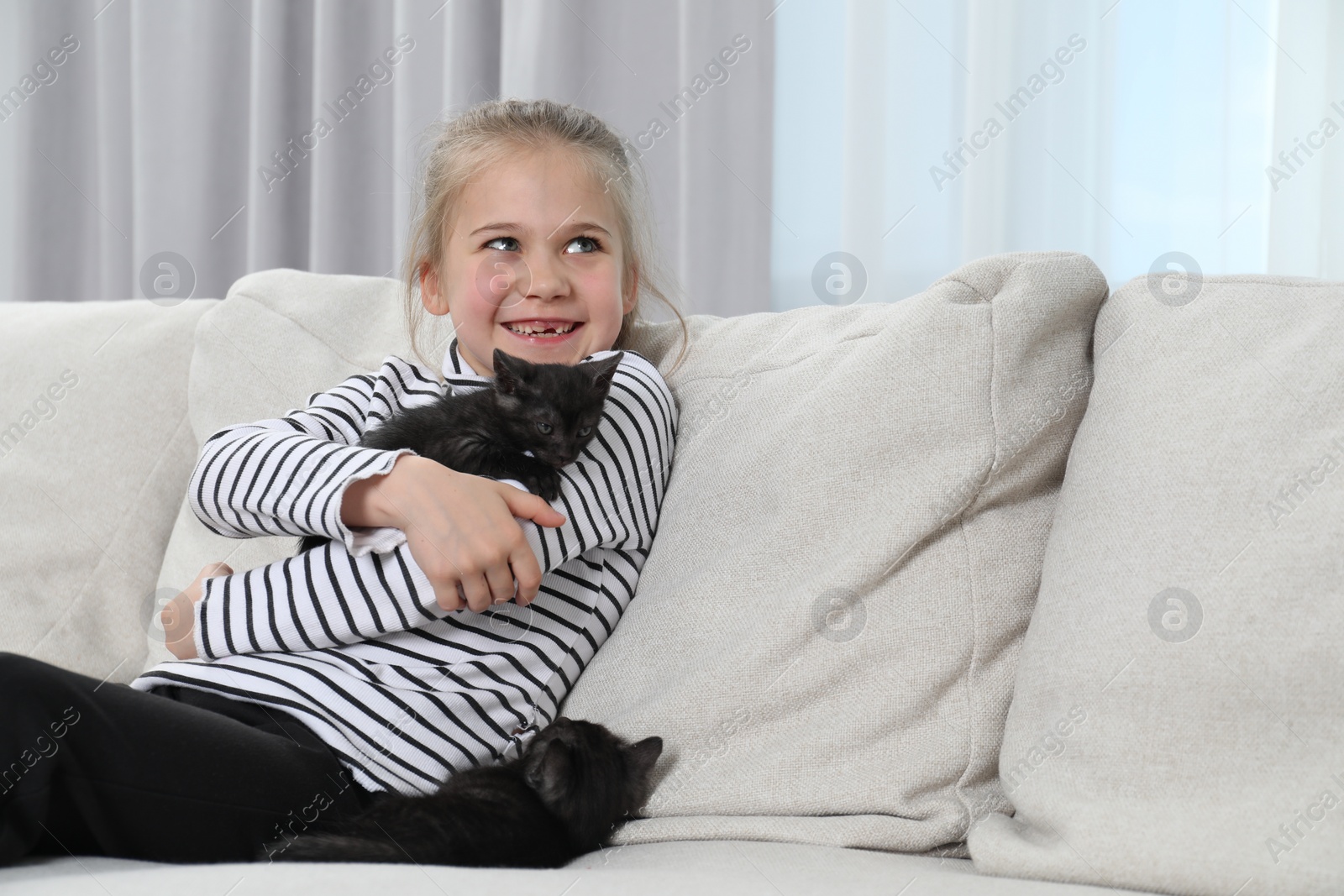 Photo of Little girl with cute fluffy kittens on sofa indoors