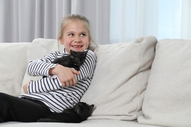 Little girl with cute fluffy kittens on sofa indoors