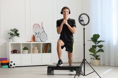 Photo of Smiling sports blogger streaming online fitness lesson with smartphone at home