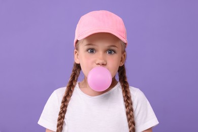 Surprised girl blowing bubble gum on purple background