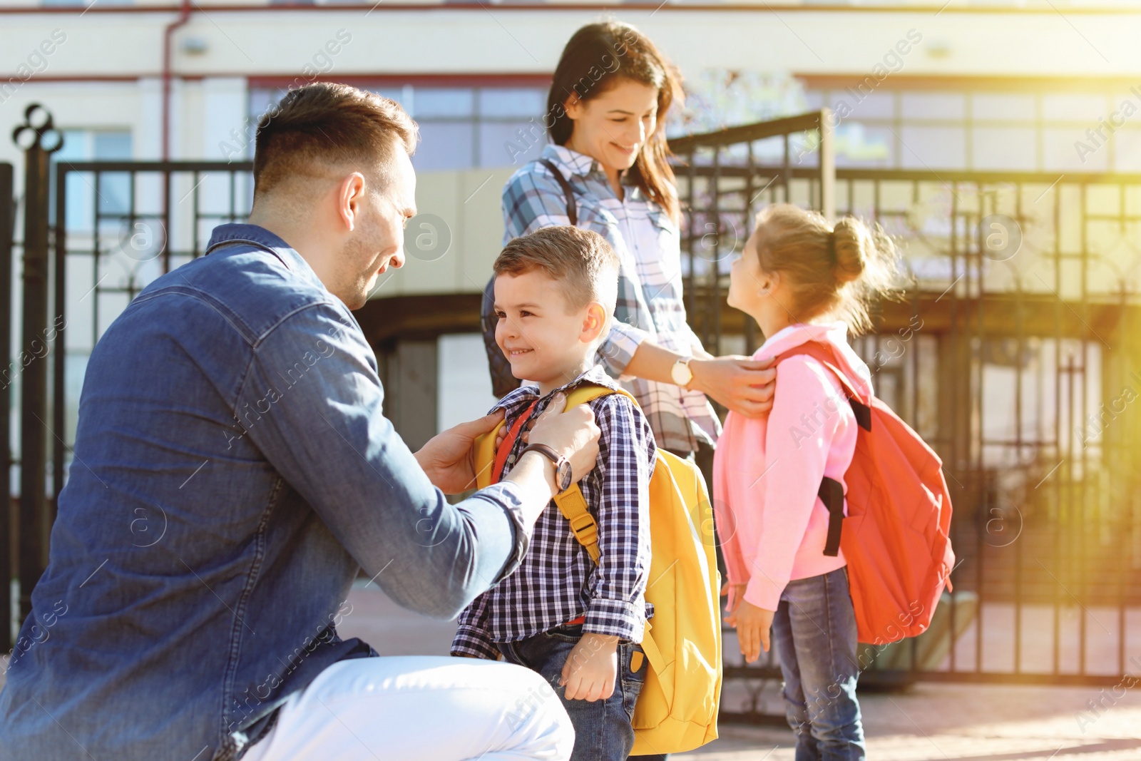 Image of Young parents saying goodbye to their little children near school