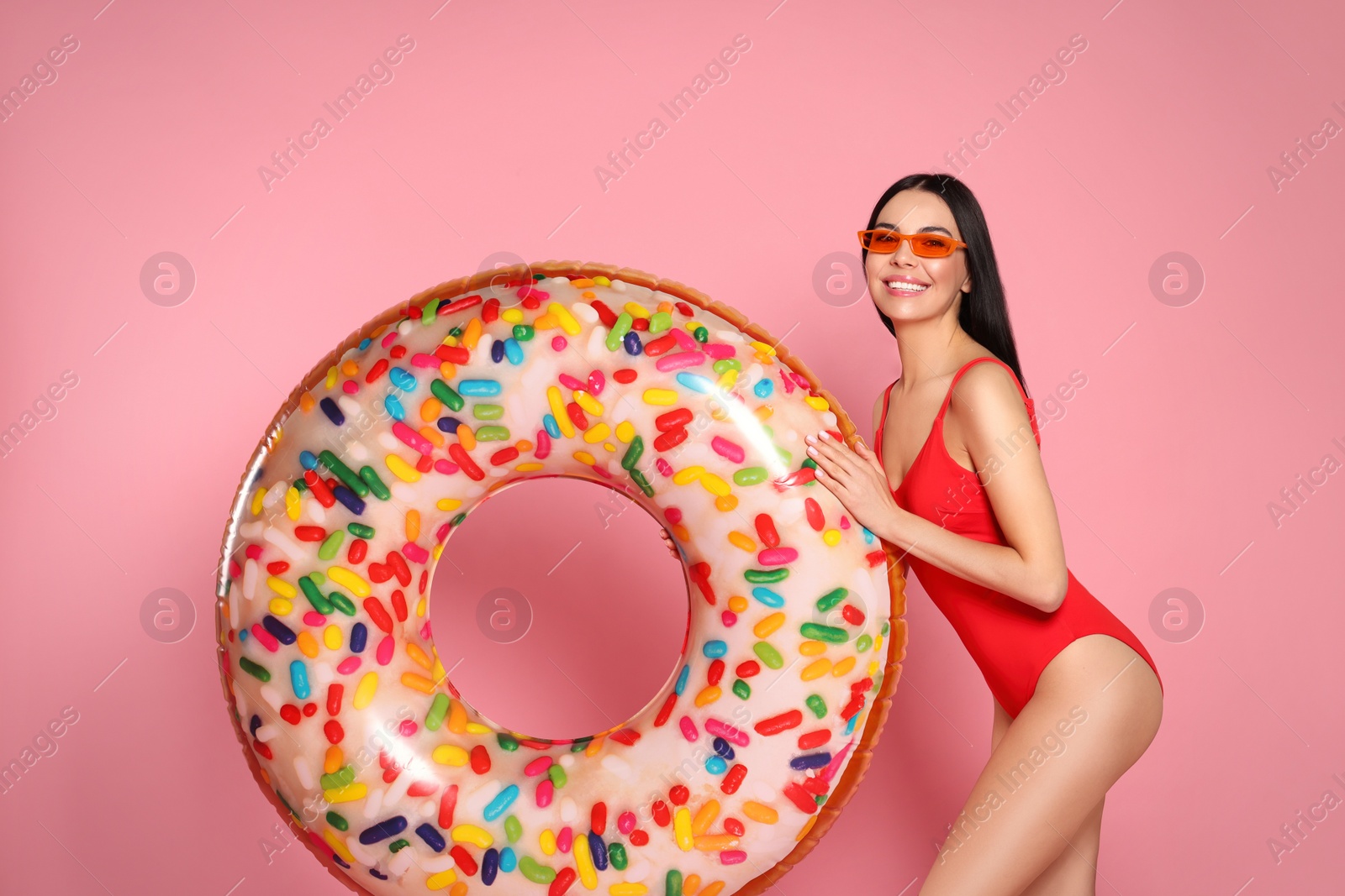 Photo of Young woman with stylish sunglasses holding inflatable ring against pink background