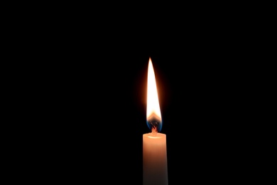 Photo of Wax candle burning on black background