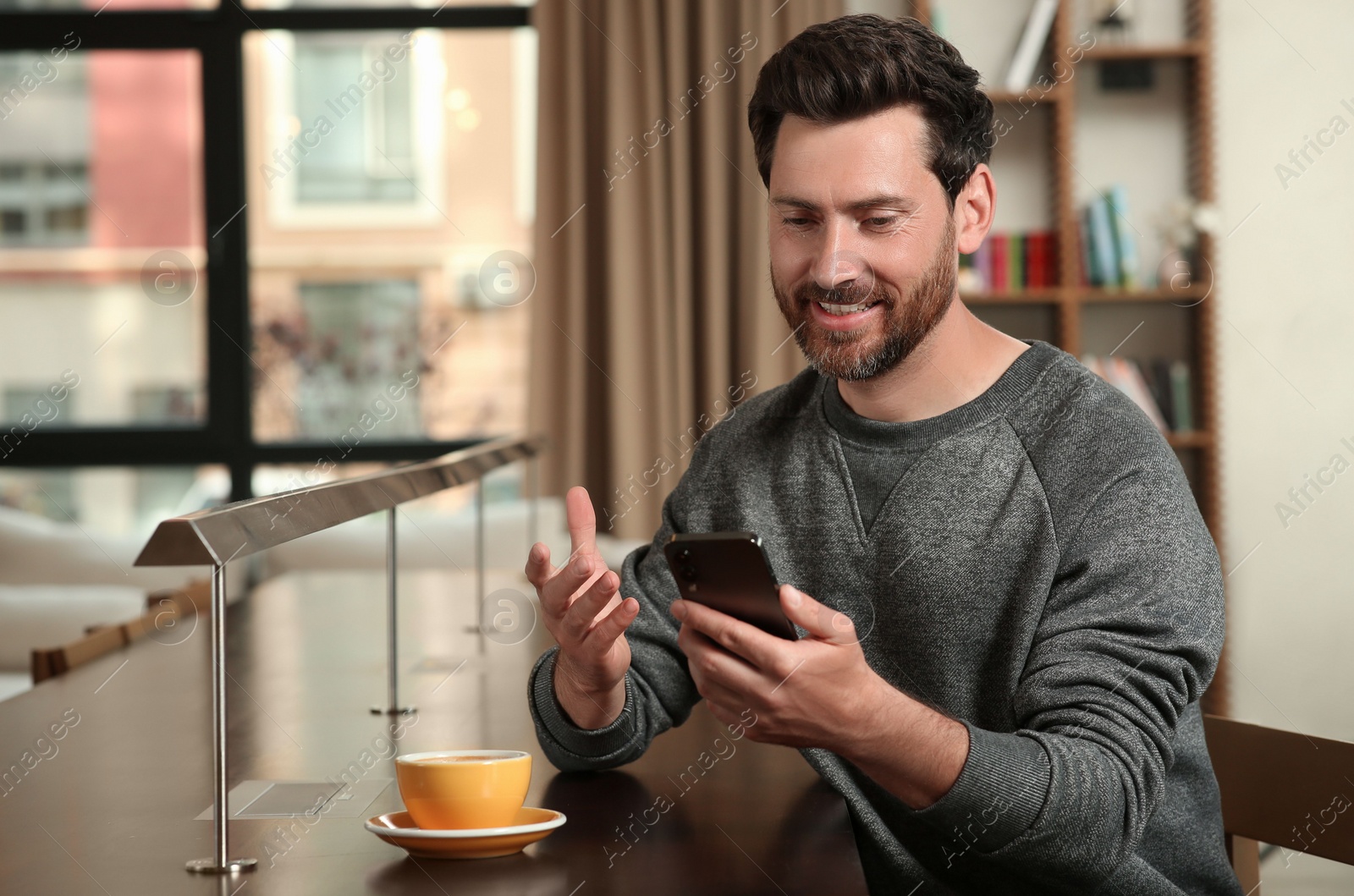 Photo of Handsome man sending message via smartphone at table indoors