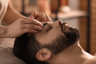 Photo of Young man receiving facial massage in beauty salon, closeup