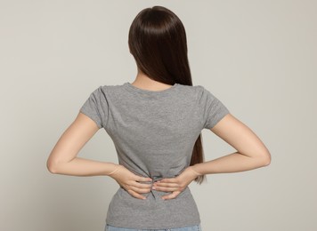 Photo of Woman suffering from back pain on light grey background. Arthritis symptoms