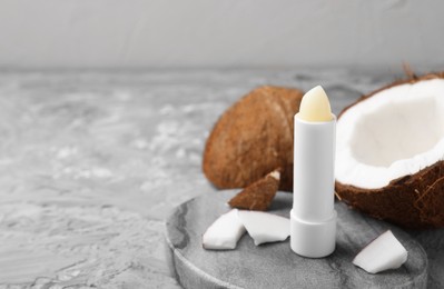 Lip balm and coconut on grey textured table, space for text