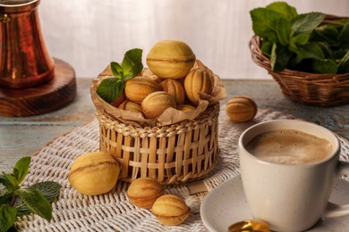 Photo of Aromatic walnut shaped cookies, mint and coffee on table. Homemade pastry filled with caramelized condensed milk