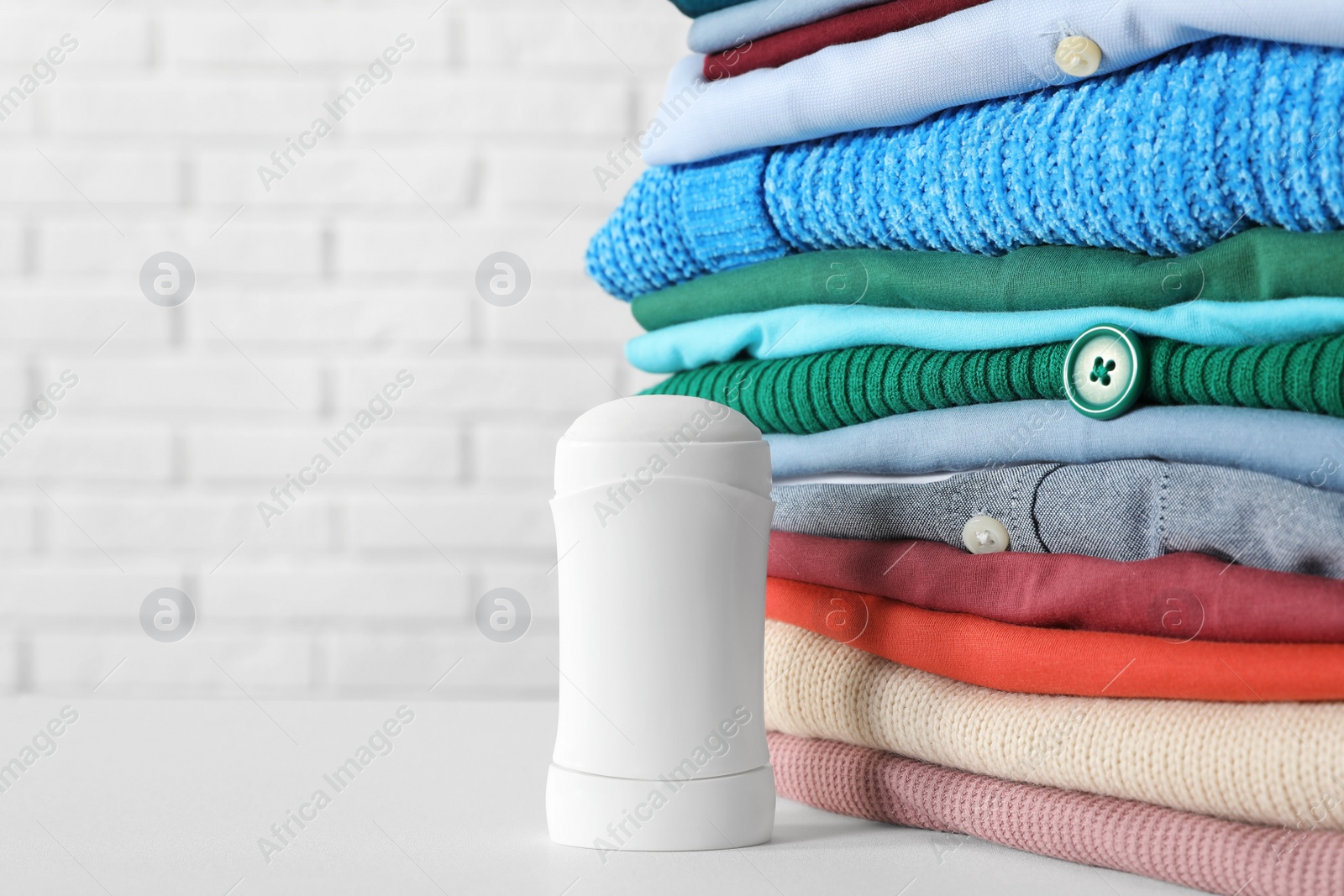 Photo of Stick deodorant near clean clothes on white table. Space for text