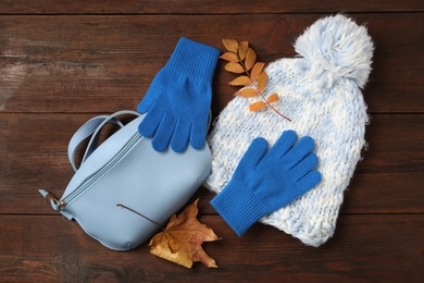 Stylish woolen gloves, hat, fanny pack and dry leaves on wooden table, flat lay