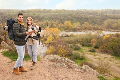 Photo of Couple of travelers with backpacks and map enjoying beautiful view near mountain river. Autumn vacation