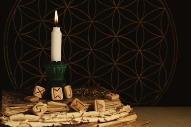 Photo of Wooden runes, old books and burning candle on grey table, space for text