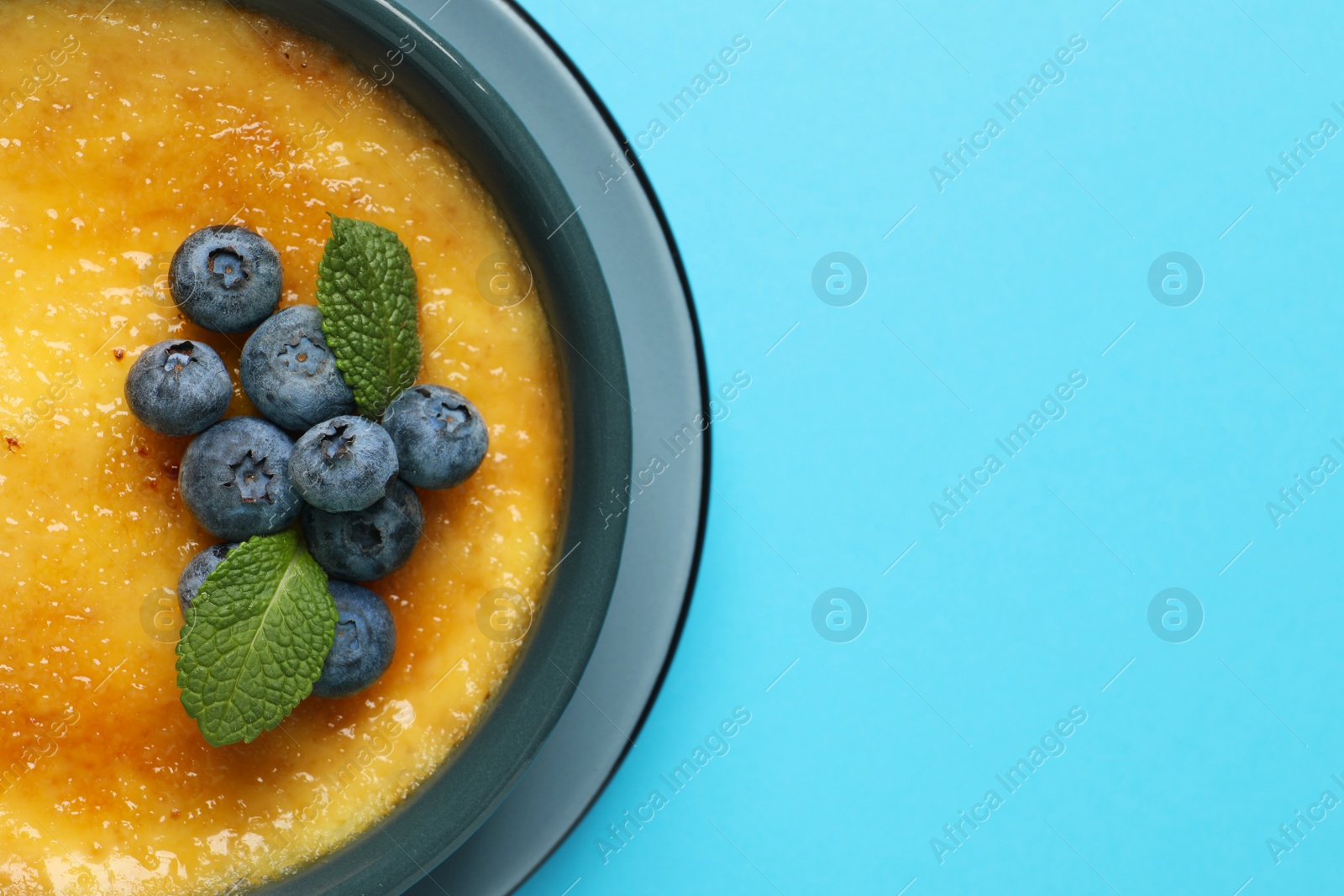 Photo of Delicious creme brulee with fresh blueberries and mint on light blue background, top view. Space for text