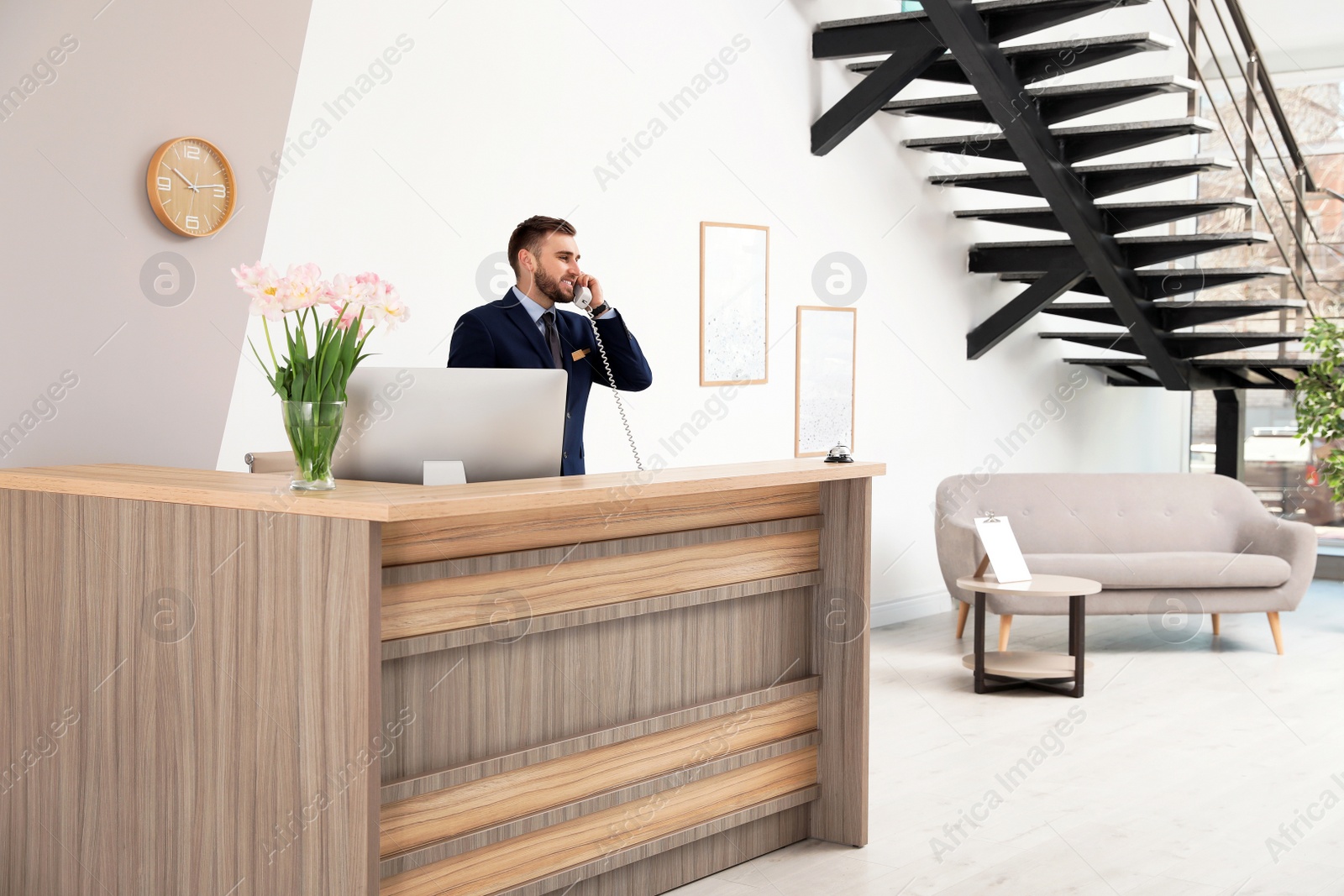 Photo of Receptionist talking on telephone at desk in modern hotel