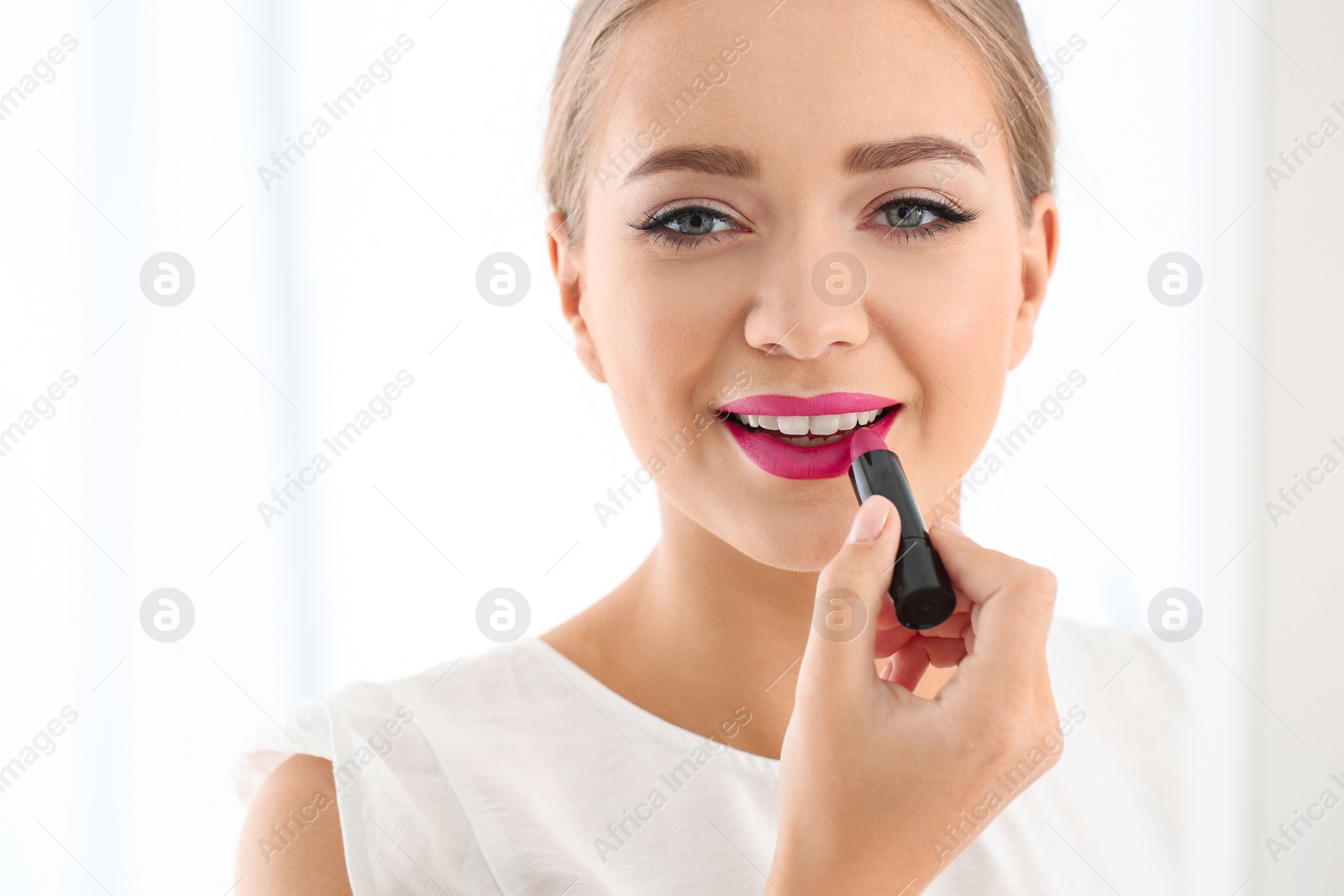 Photo of Beautiful woman applying lipstick on light background