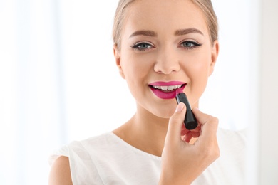 Beautiful woman applying lipstick on light background