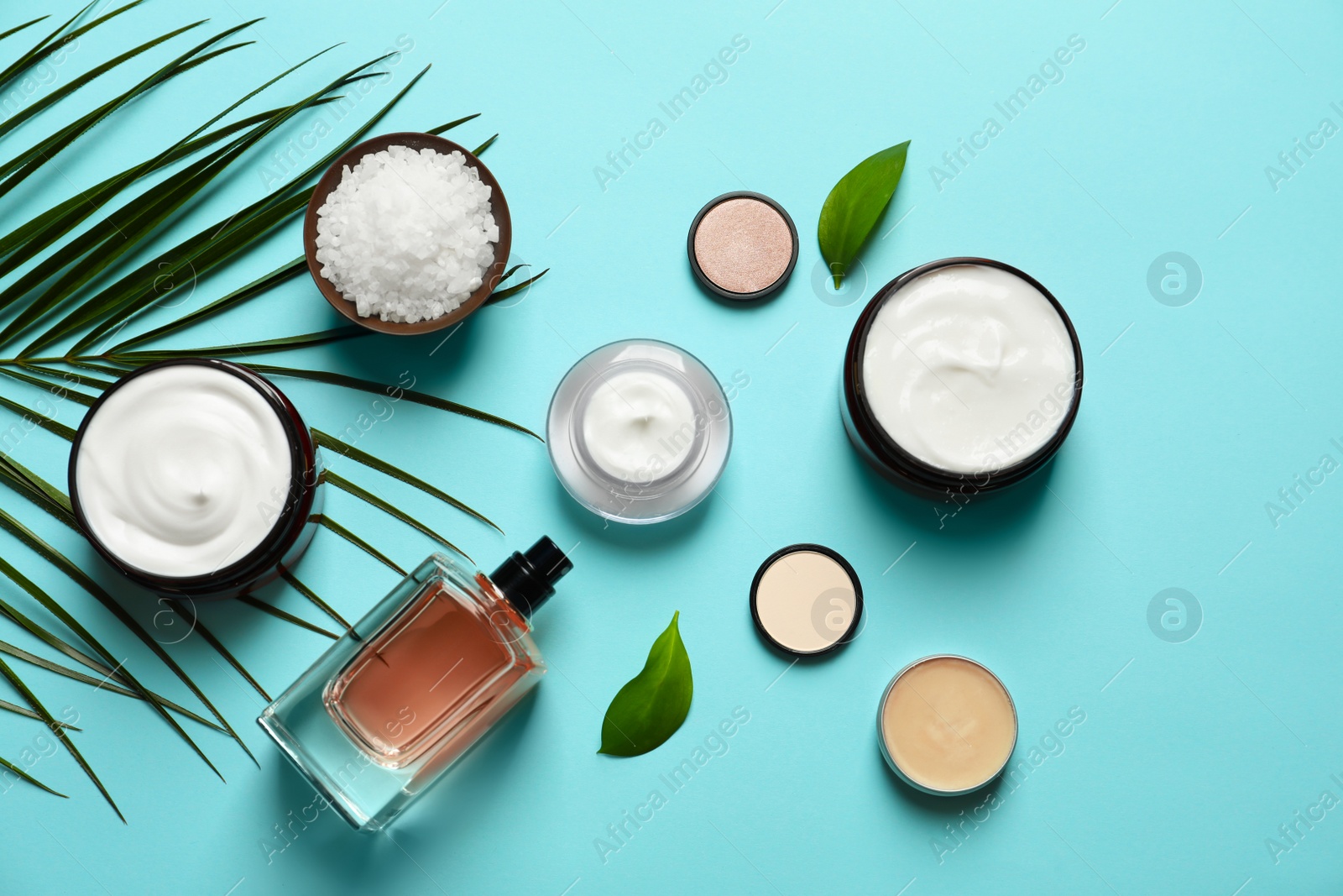 Photo of Different skin care cosmetic products with green leaves on color background, top view