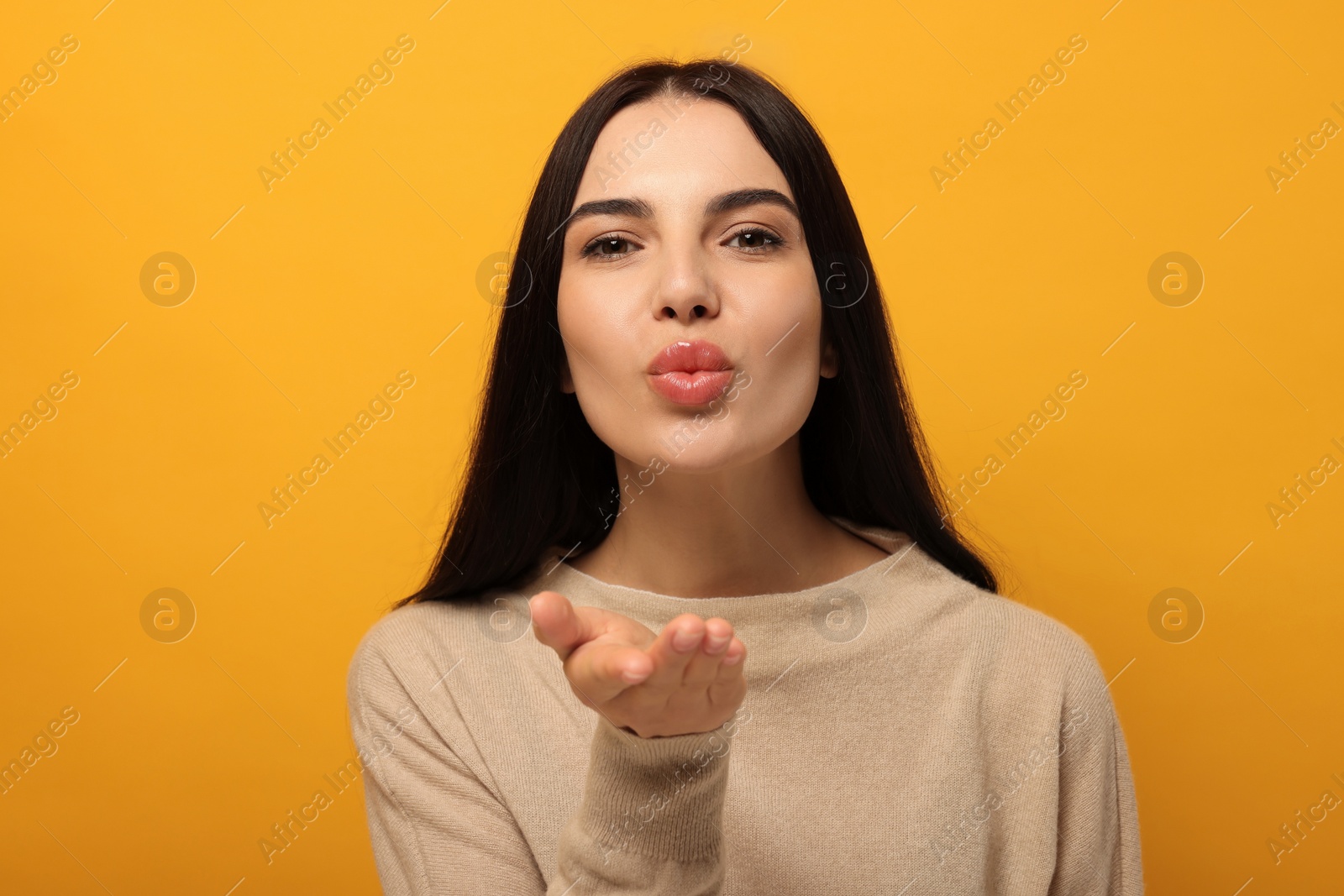 Photo of Beautiful young woman blowing kiss on orange background