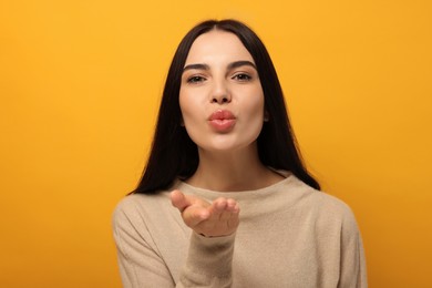 Beautiful young woman blowing kiss on orange background