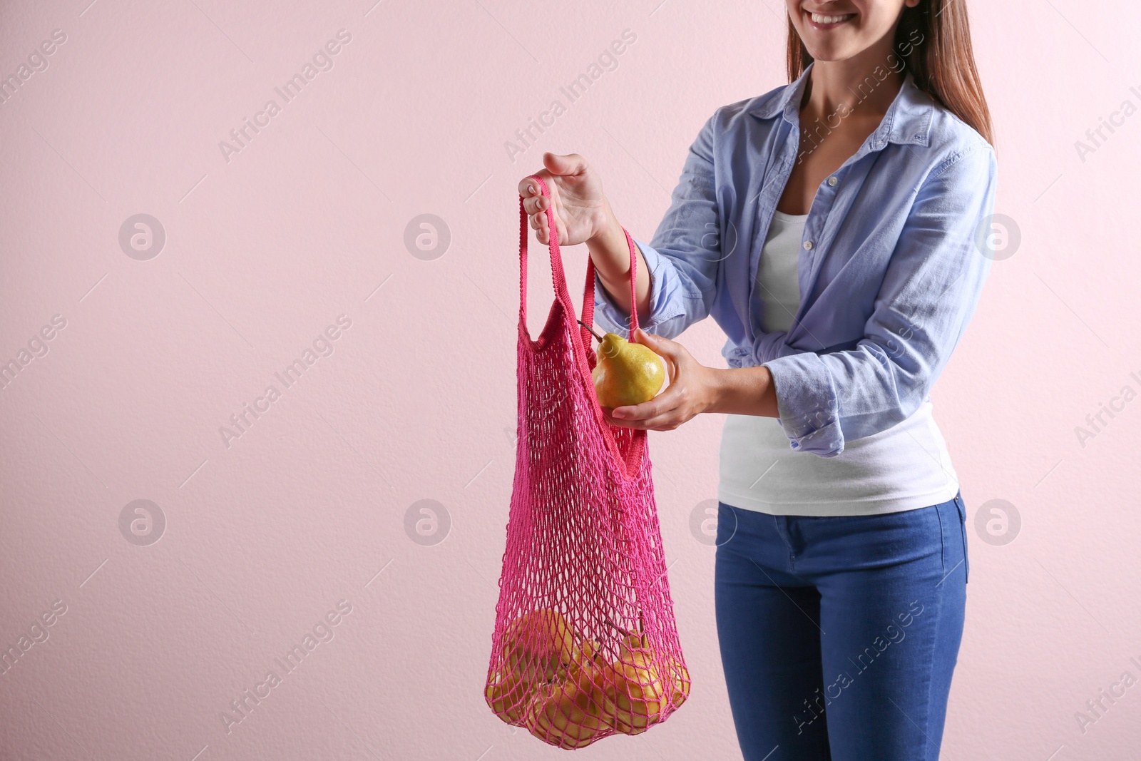 Photo of Woman holding net bag with fresh ripe pears on pink background, closeup