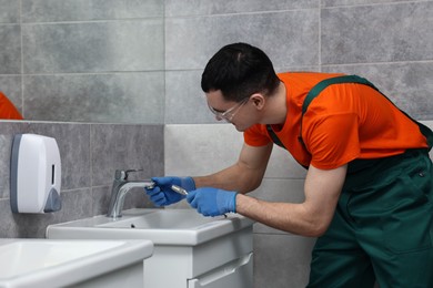 Young plumber repairing metal faucet in bathroom