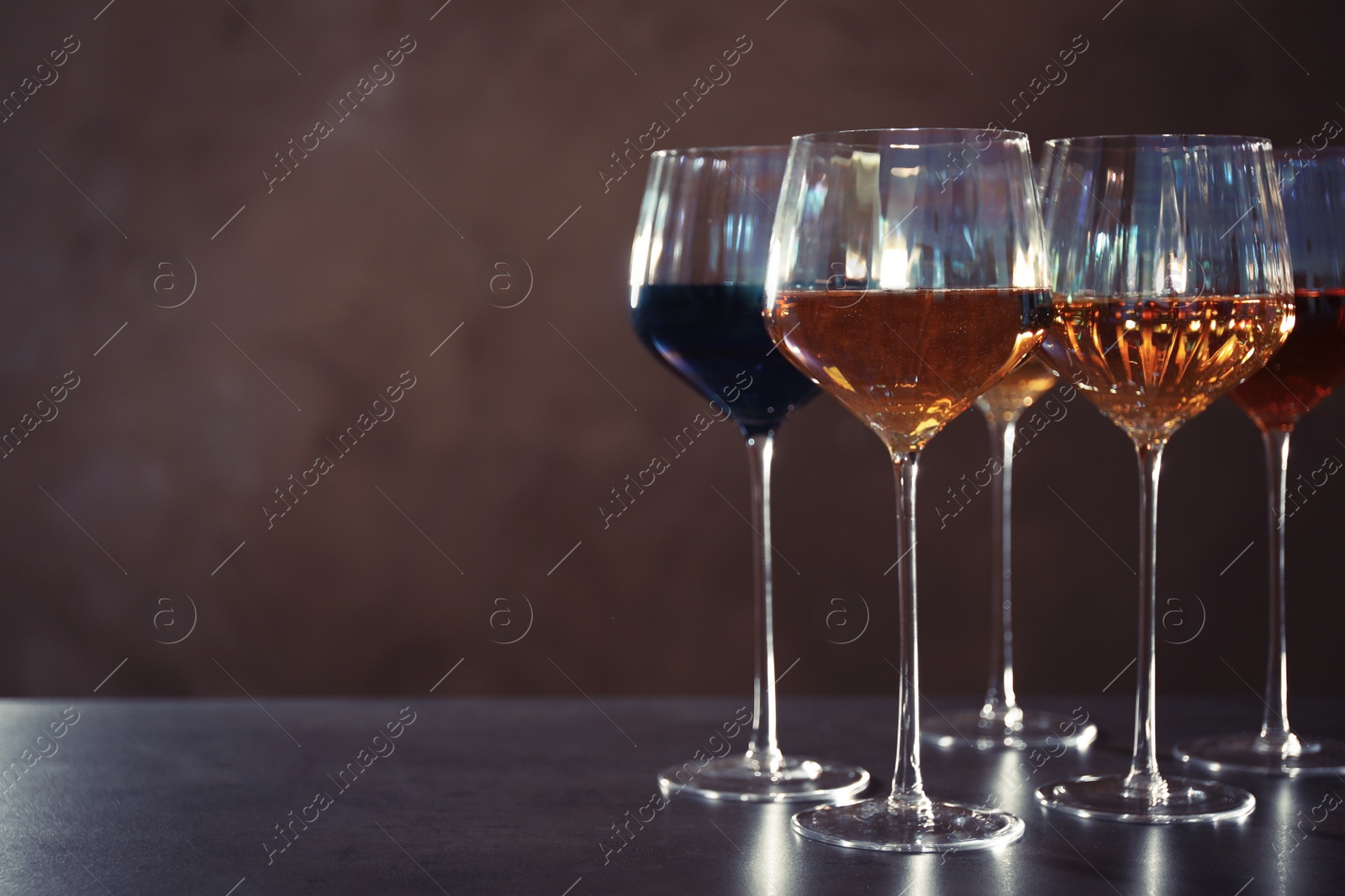 Photo of Elegant glasses with different wines on table against brown background